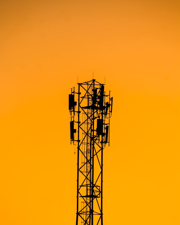 hero-services A telecommunication tower silhouetted against a vibrant orange sunset sky in India.